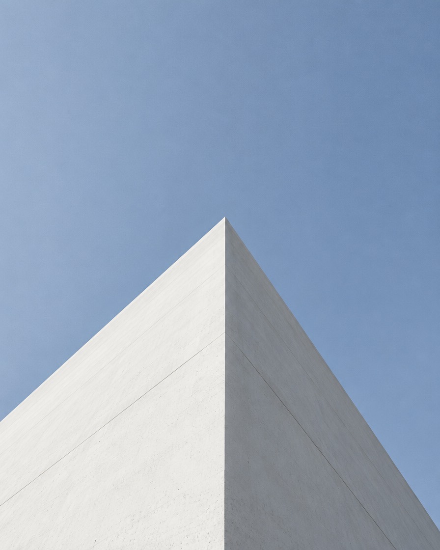 Looking up the clean edge of a white concrete building into open sky
